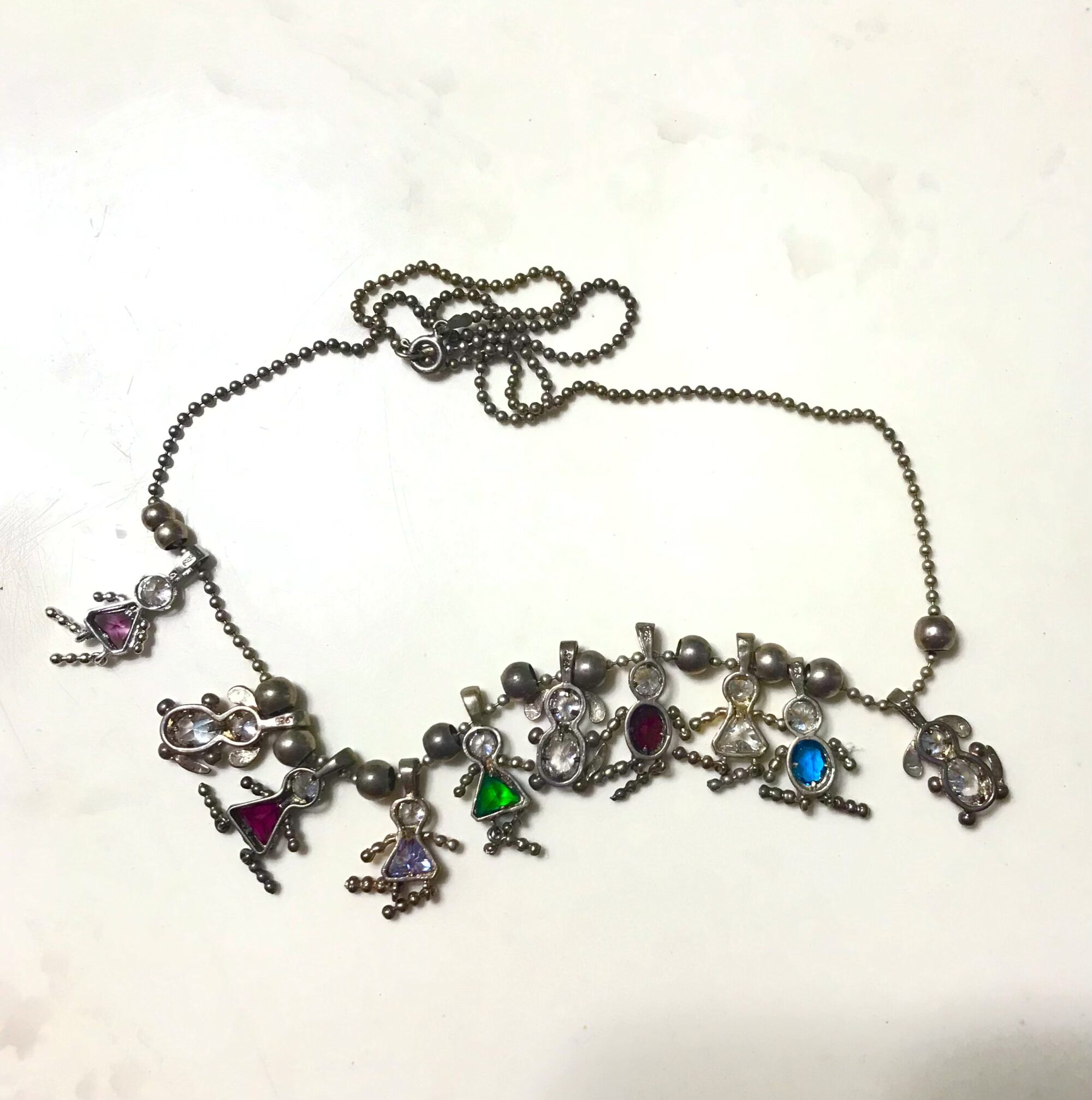Photo of a long necklace bearing nine charms in the shape of people and one charm in the shape of a dog.