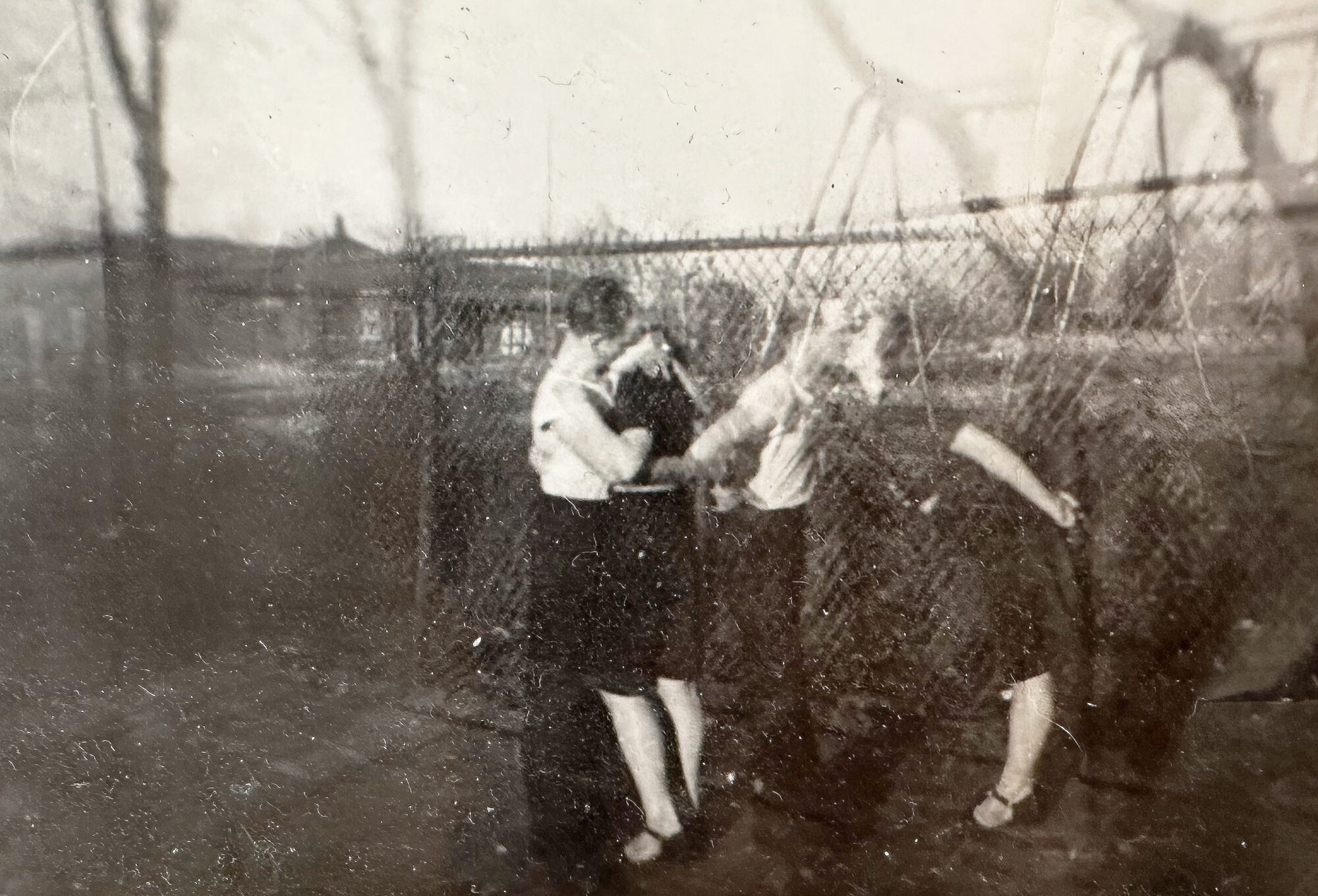Black and white photo of a man and woman kissing next to a chainlink fence.