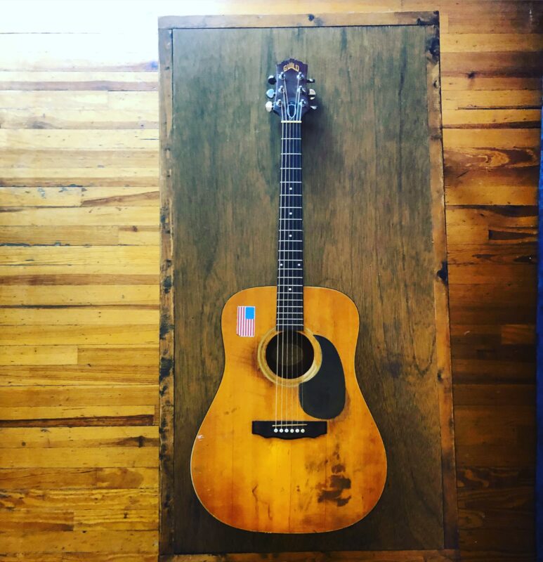 Photo of an acoustic guitar hanging on a wall.