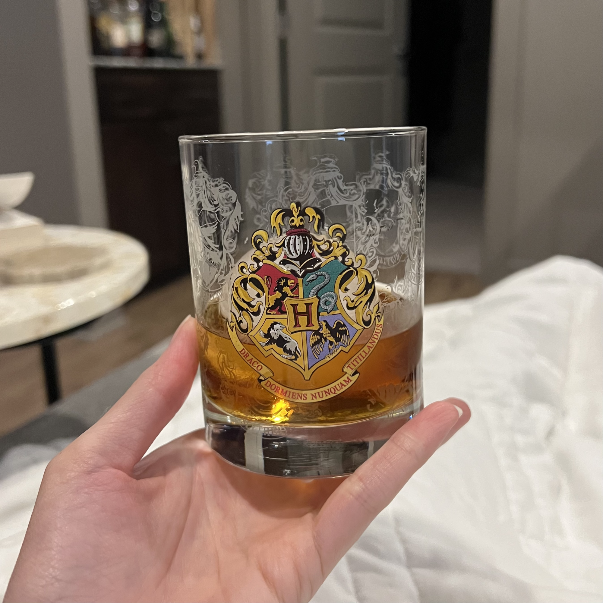 Photo of a hand holding a small bourbon glass decorated with a Hogwarts emblem.