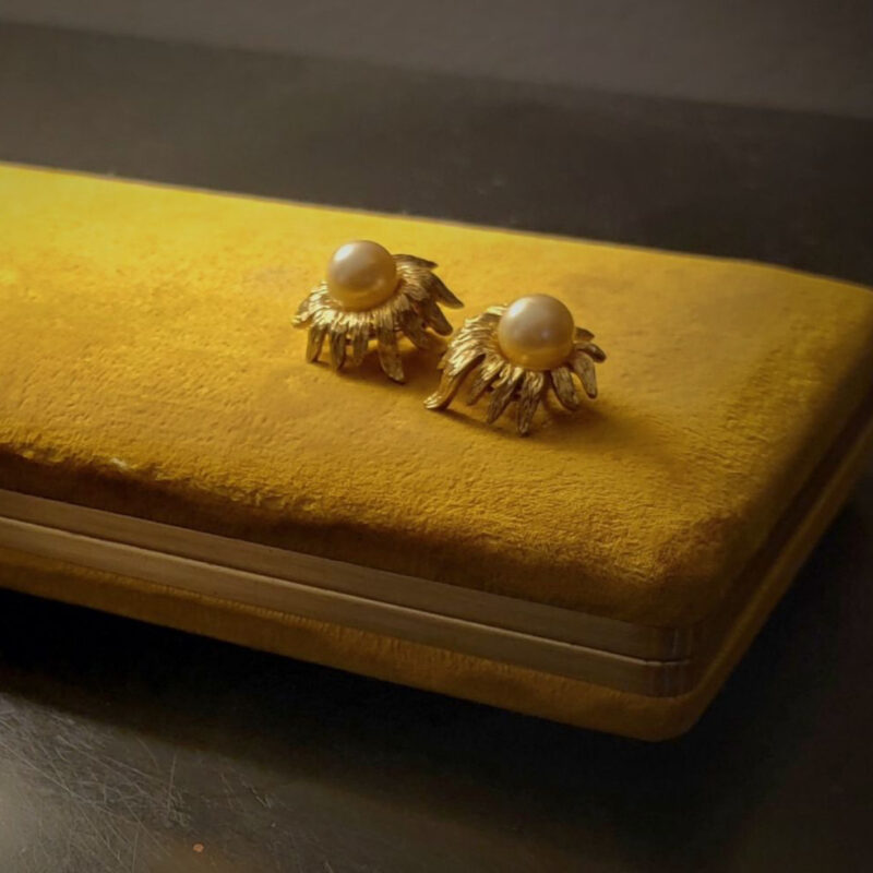 Photo of pearl earrings in a gold starburst setting sitting on top of a yellow velvet box.