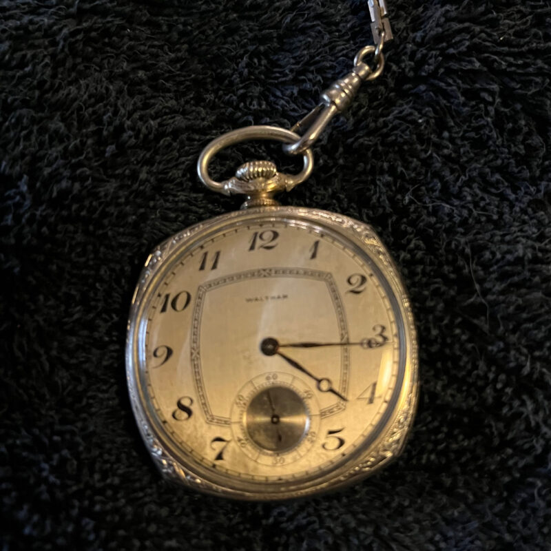 Photo of a brass pocket watch on a black background.