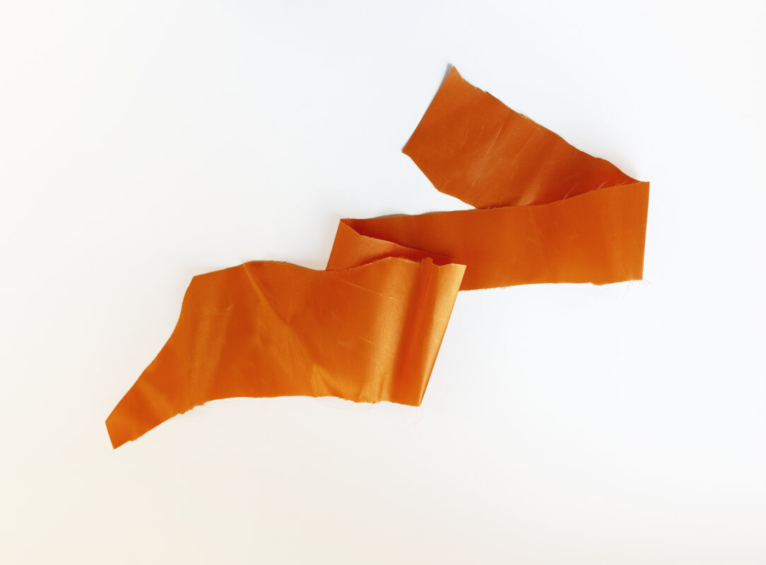 Photo of a torn piece of orange ribbon on a white surface.