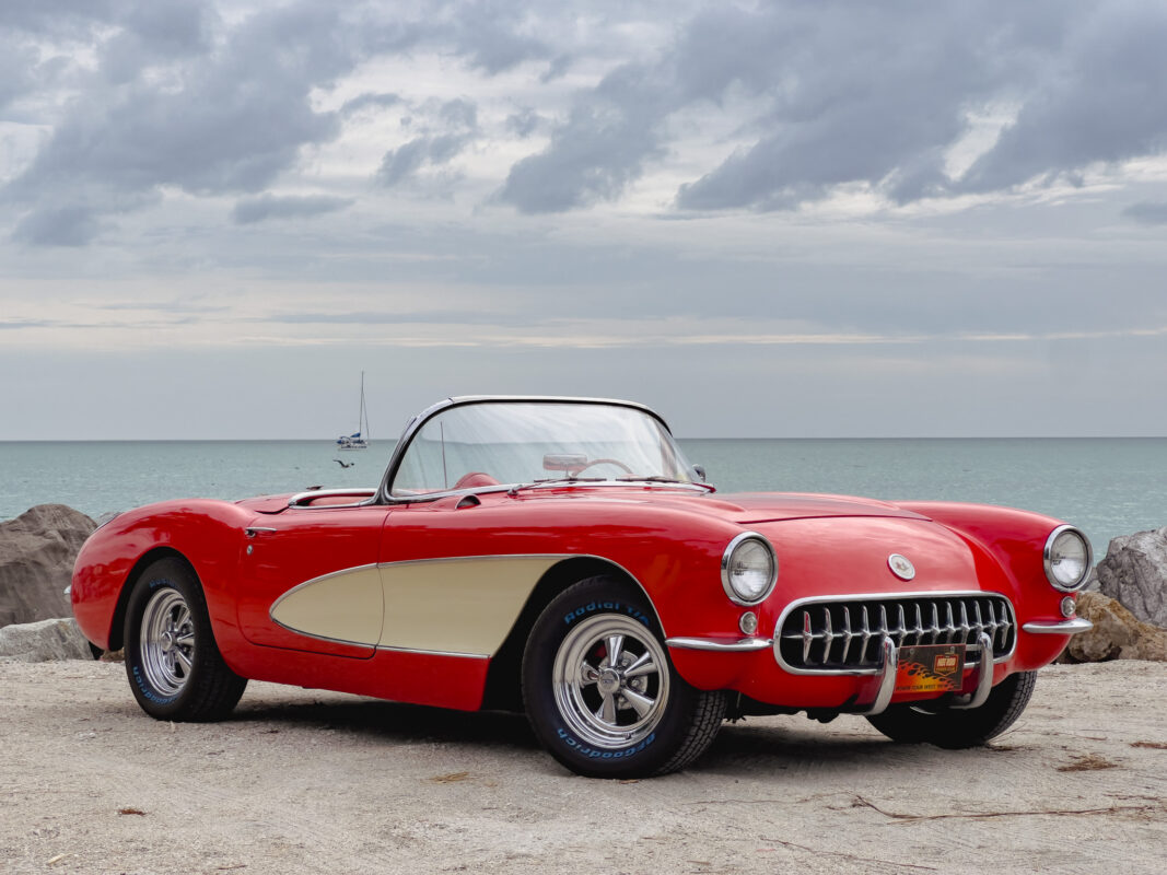 Photo of an antique red convertible with the top down parked on a beach with the ocean in the background.