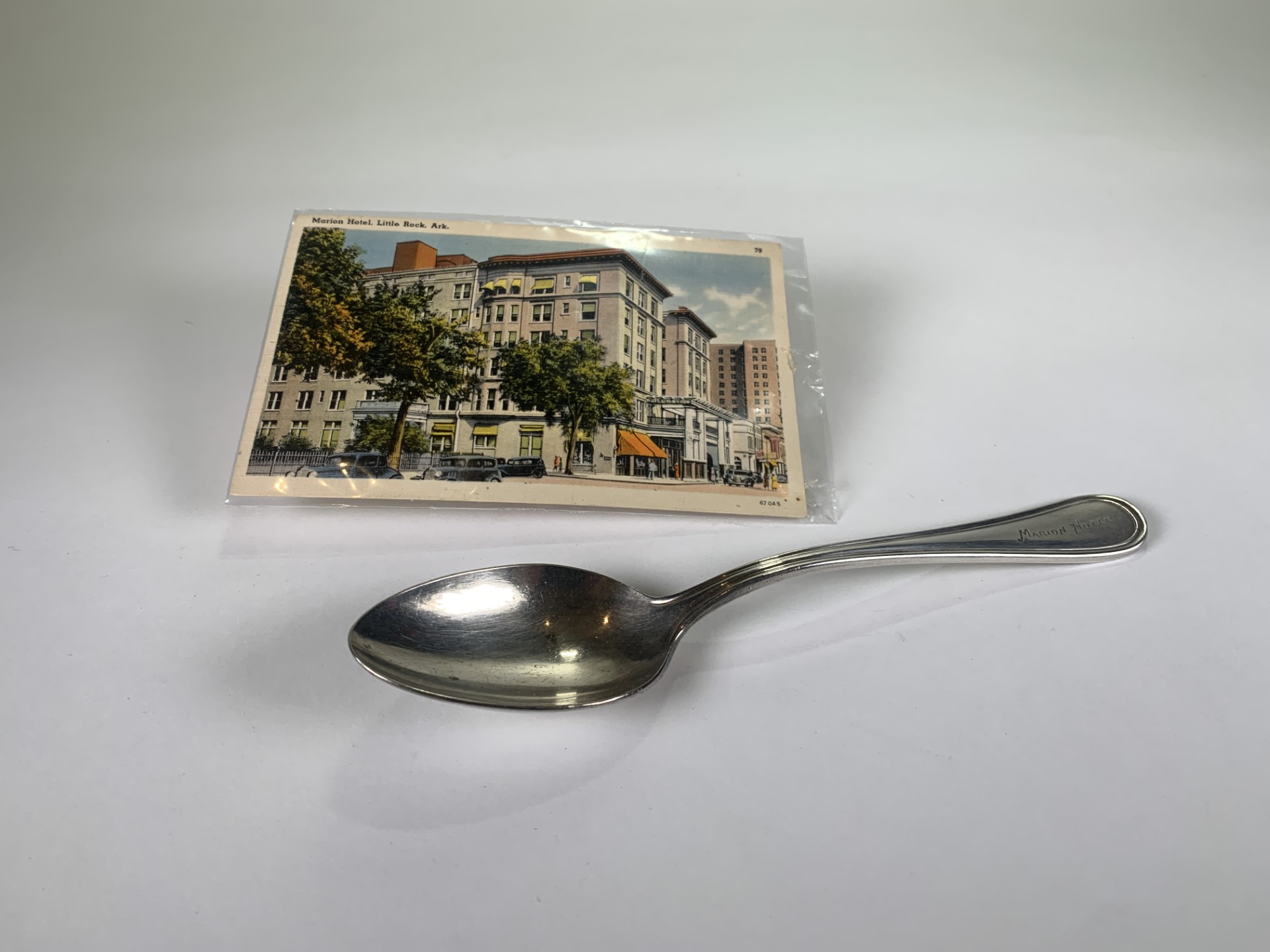 Photo of a small spoon laying on a white surface next to a postcard featuring a picture of building.