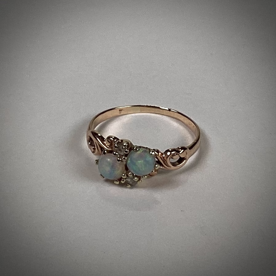 Photo of a gold wedding ring with two offset bluish-green opals in the center.